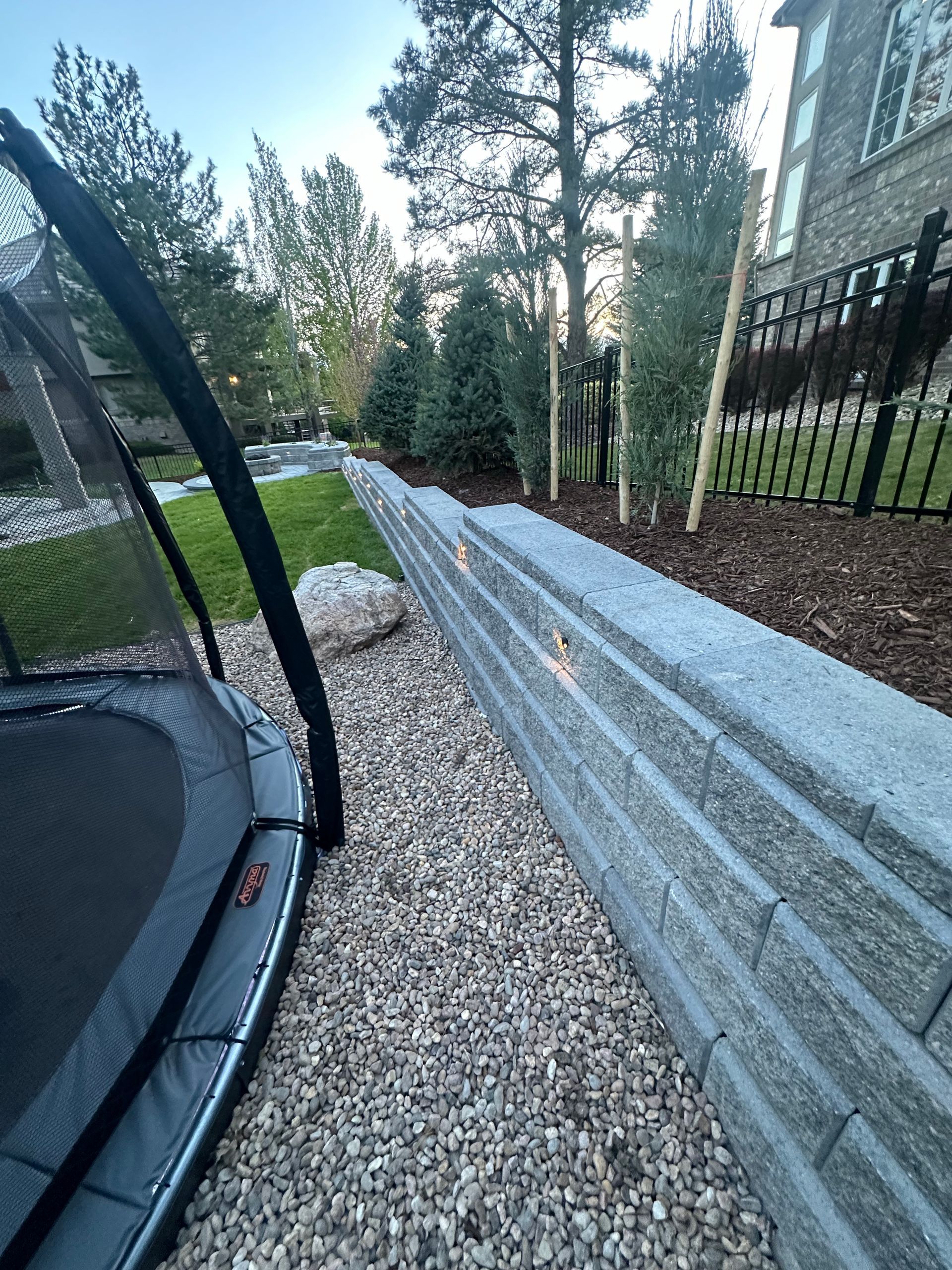 A trampoline is sitting next to a stone wall in a backyard.
