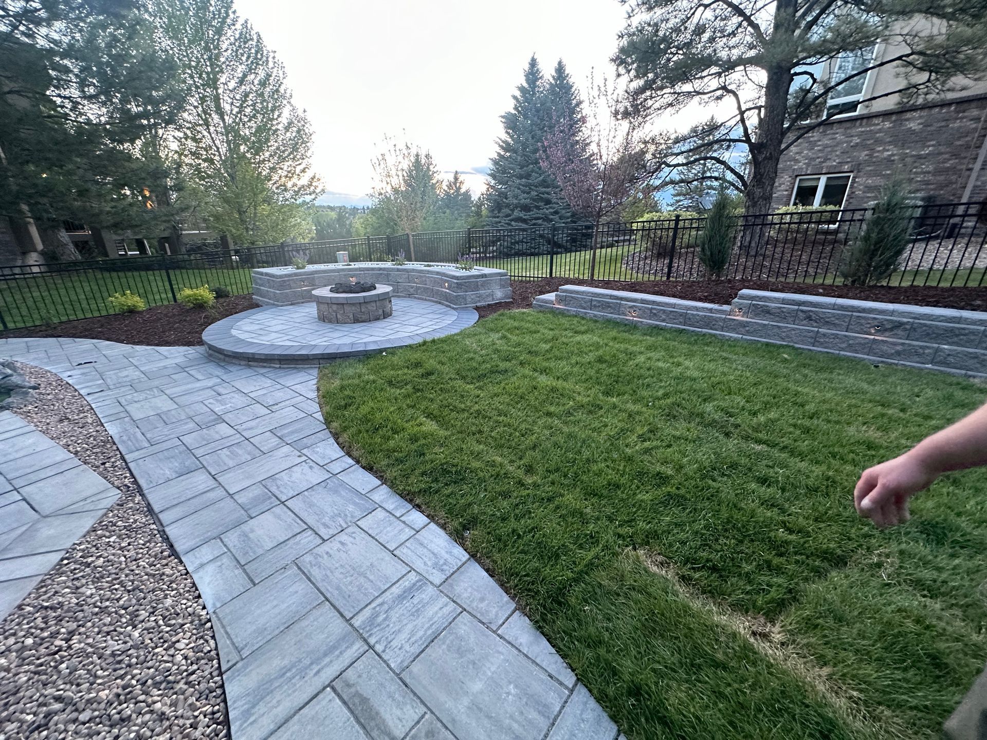 A person is walking down a path in a backyard with a fire pit.