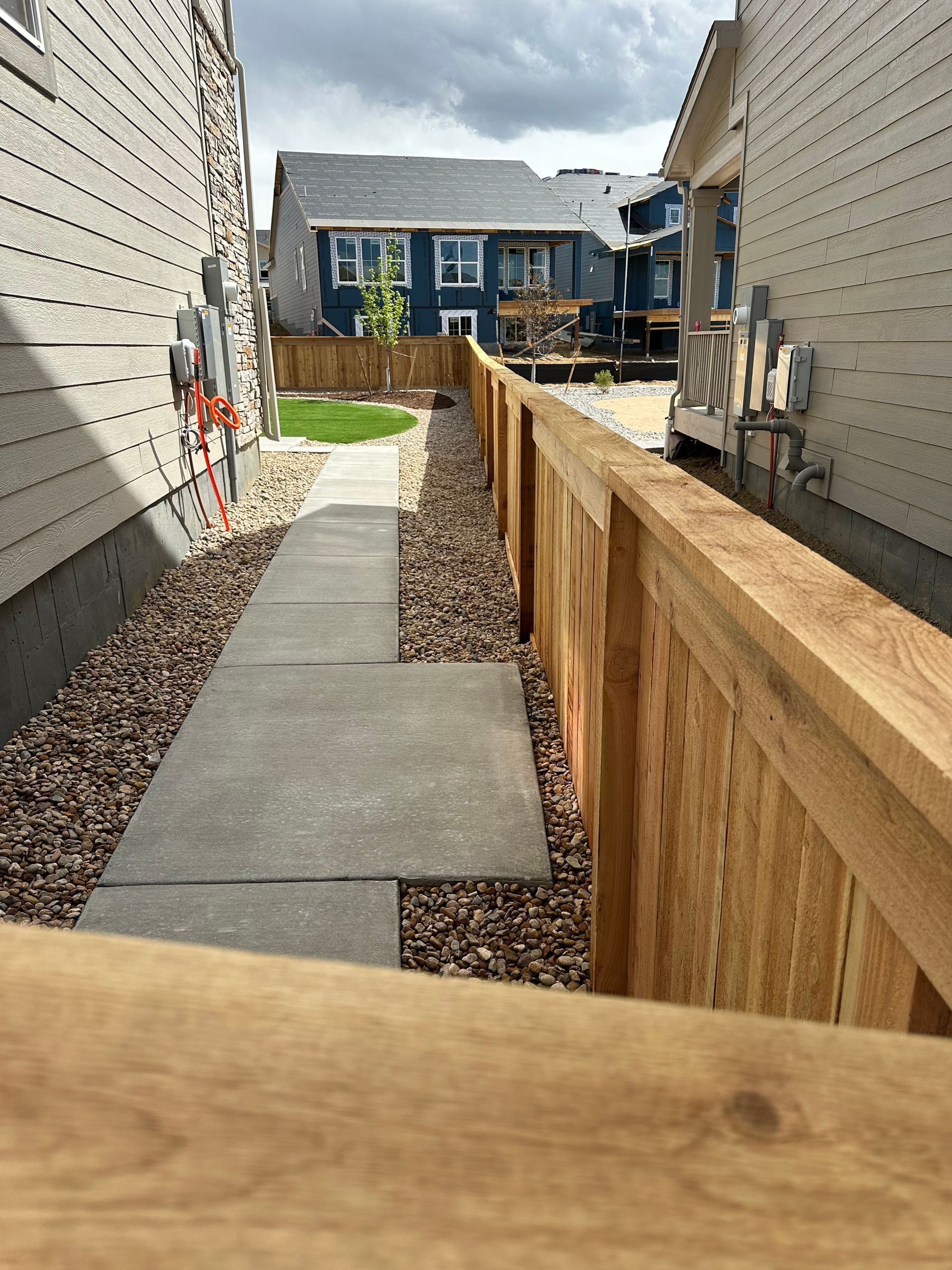A wooden fence surrounds a concrete walkway between two houses.