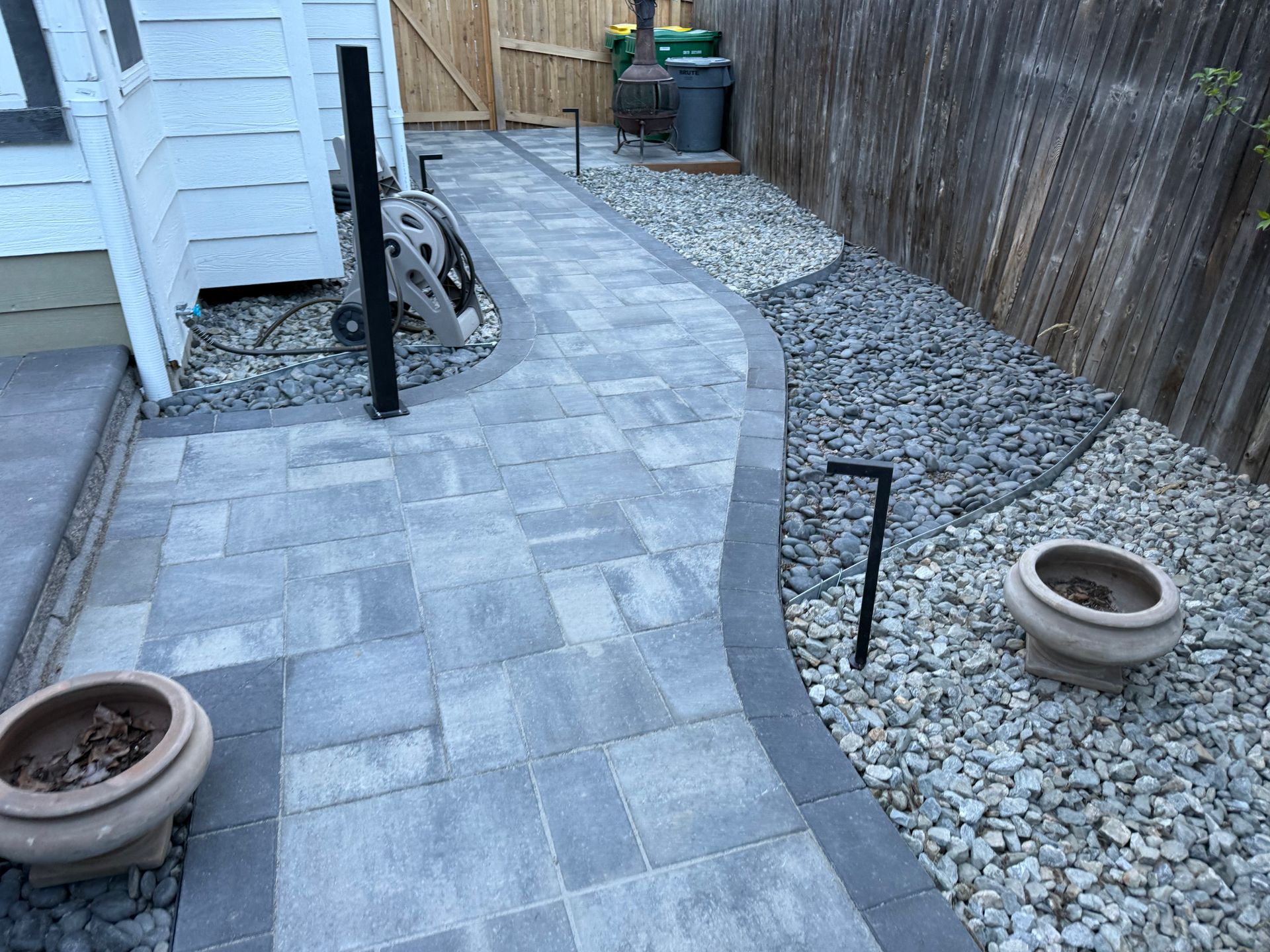 A stone walkway leading to a house with a fence in the background.