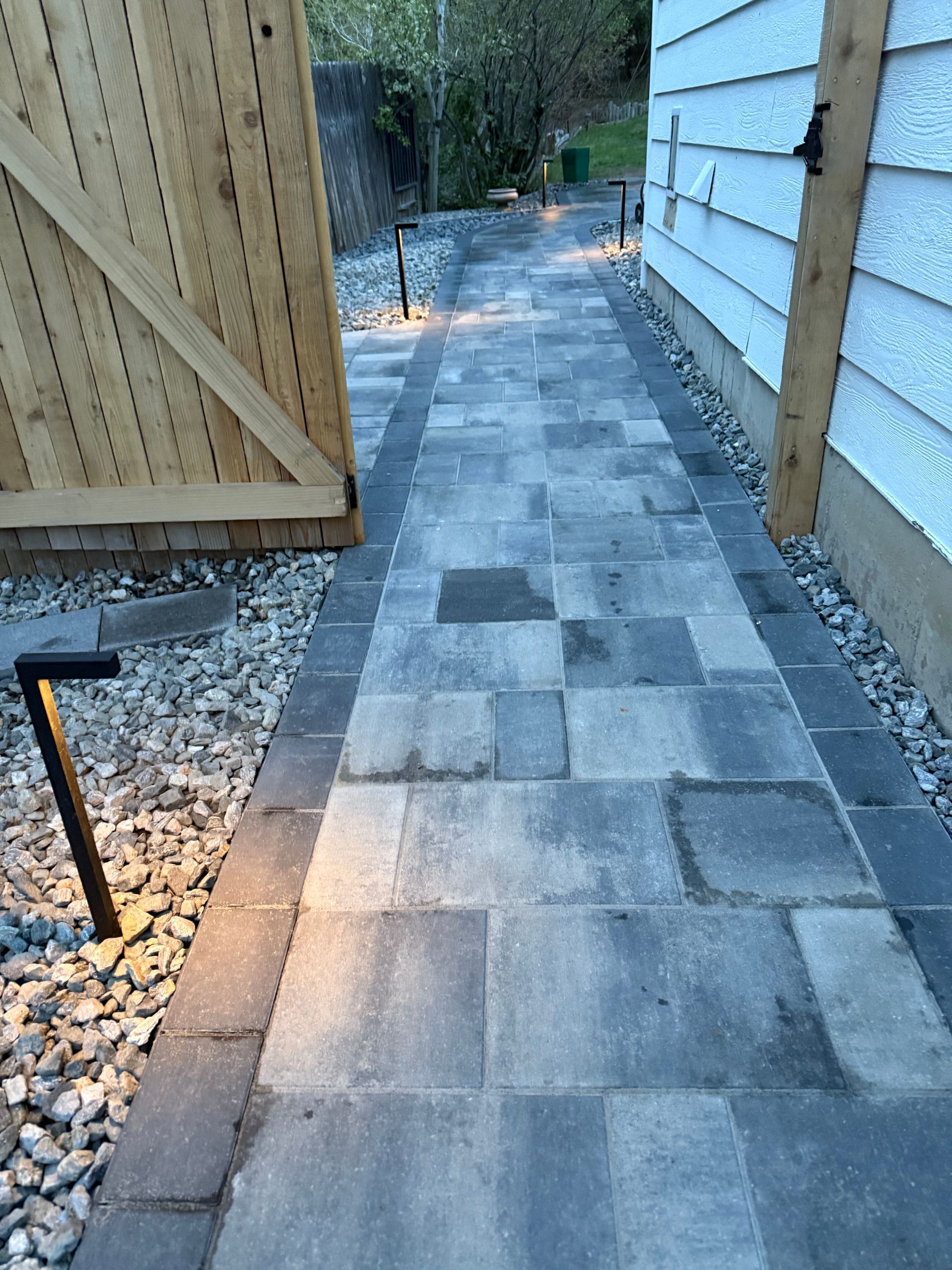 A brick walkway leading to a house with a wooden fence.