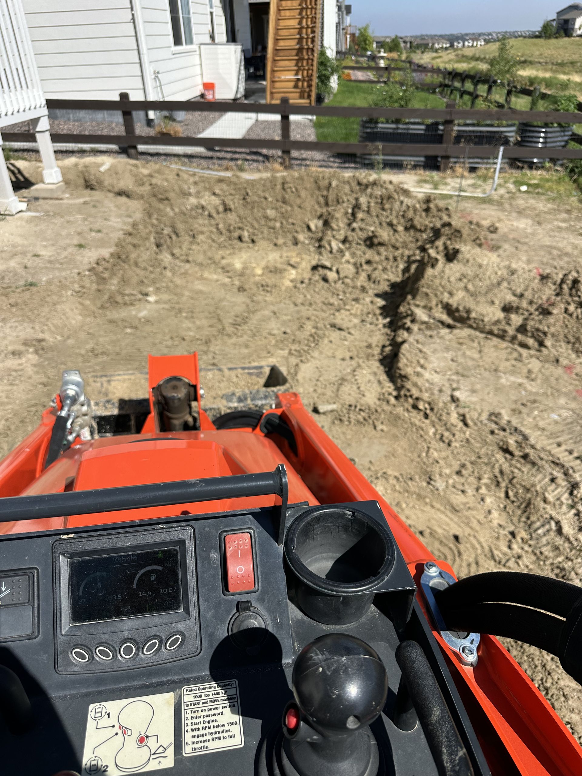 A person is driving an orange tractor on a dirt road.