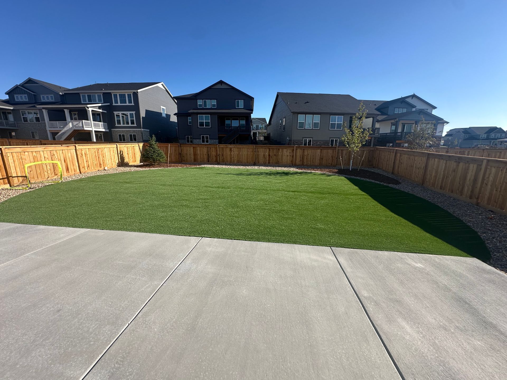 A large lawn with a wooden fence and houses in the background