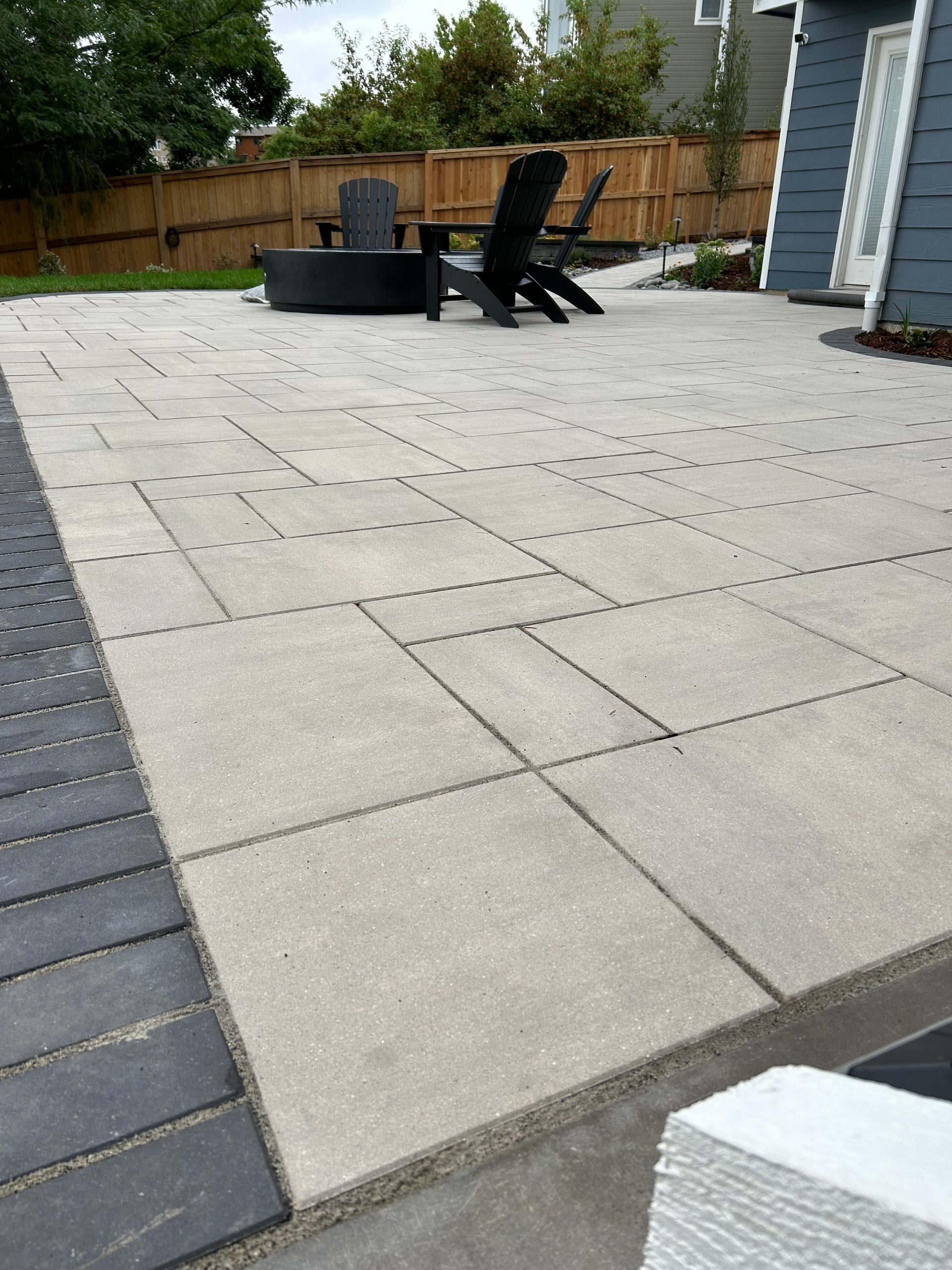 A patio with chairs and a table in the backyard of a house.