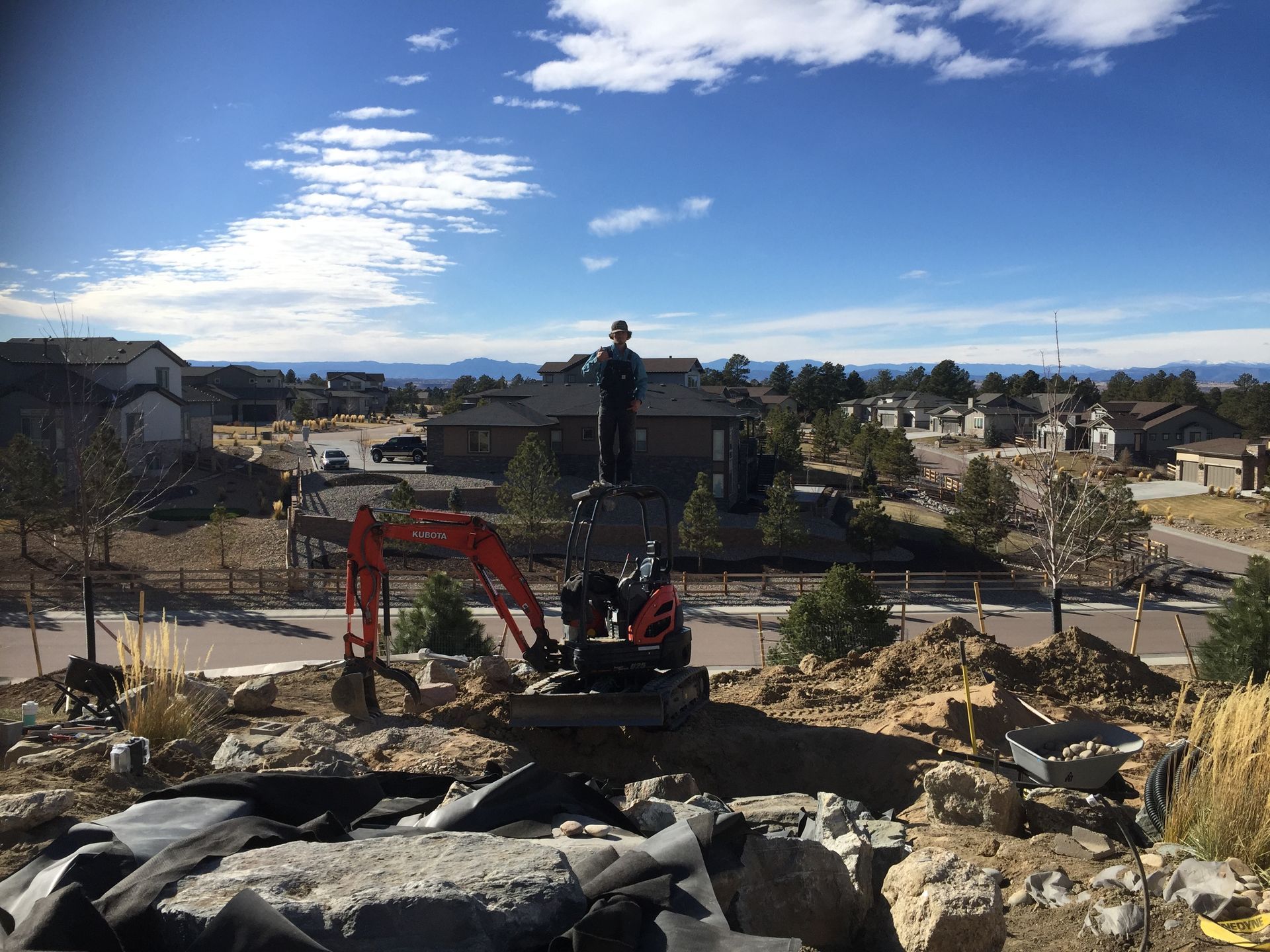 A man is standing on top of a pile of rocks next to an excavator.