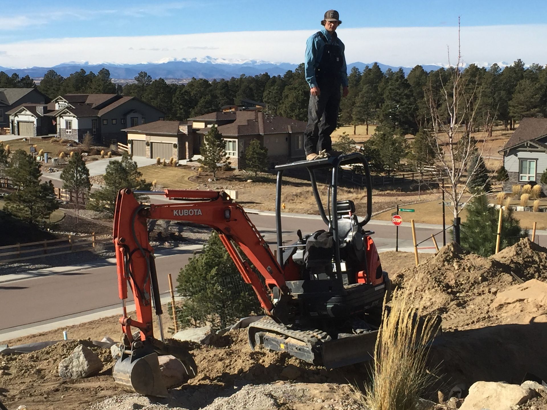 A man is standing on top of an excavator in a dirt field.