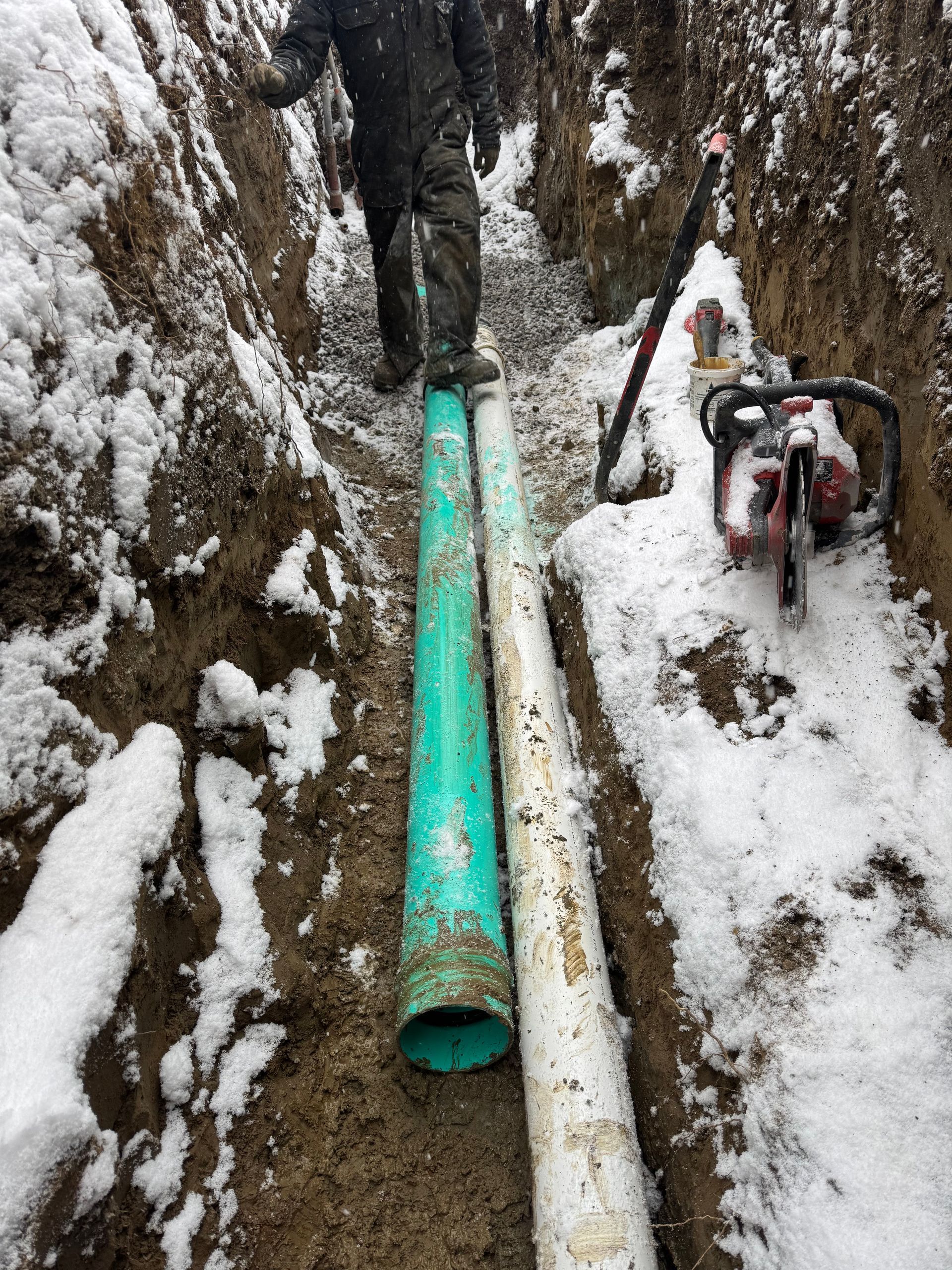 Un homme se tient à côté d'un tuyau vert dans une tranchée enneigée.