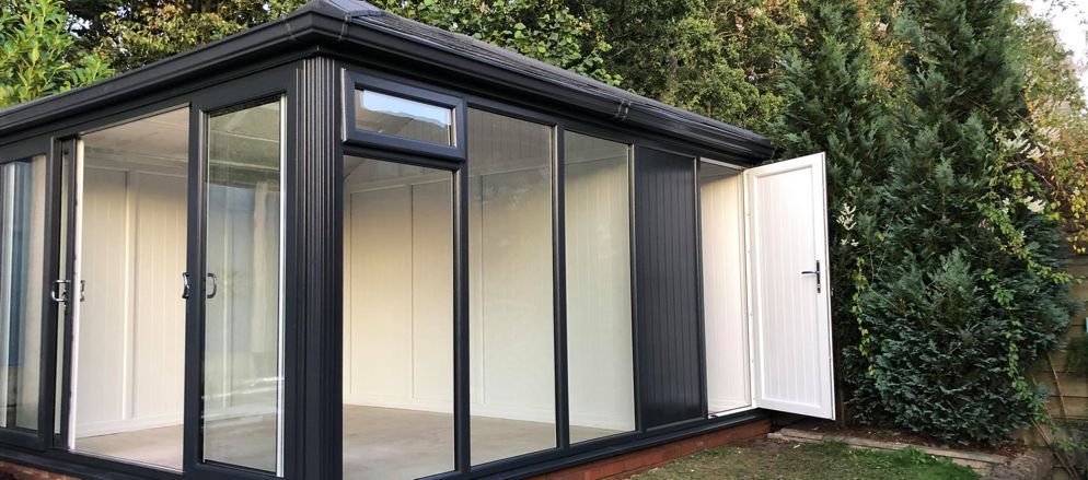 A small black house with sliding glass doors is sitting in the middle of a lush green yard.