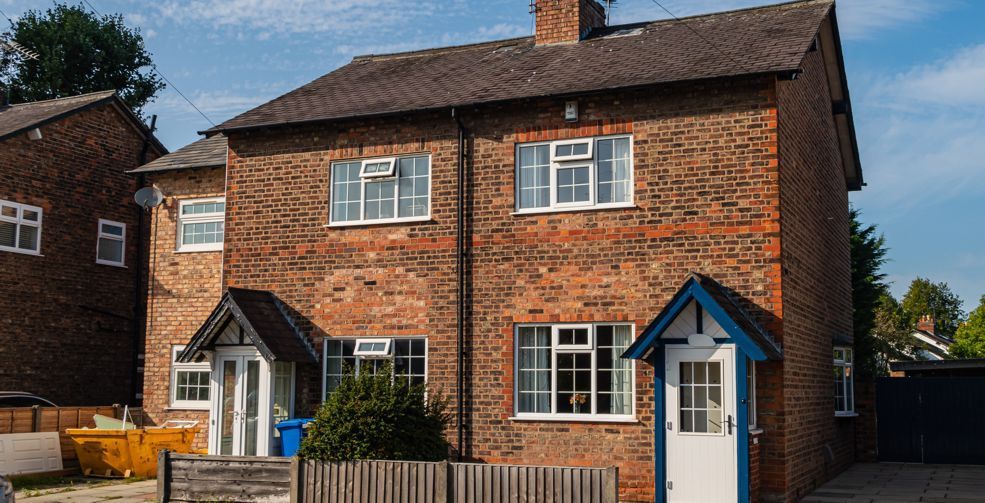 A brick house with white windows and a blue fence in a residential area.