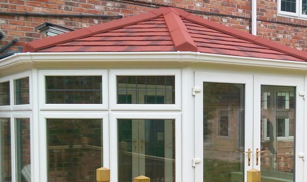 A conservatory with a red tiled roof and white windows.