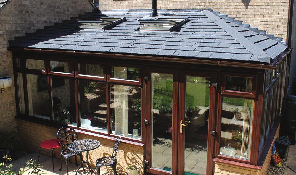 A conservatory with a black roof and a table and chairs in front of it.