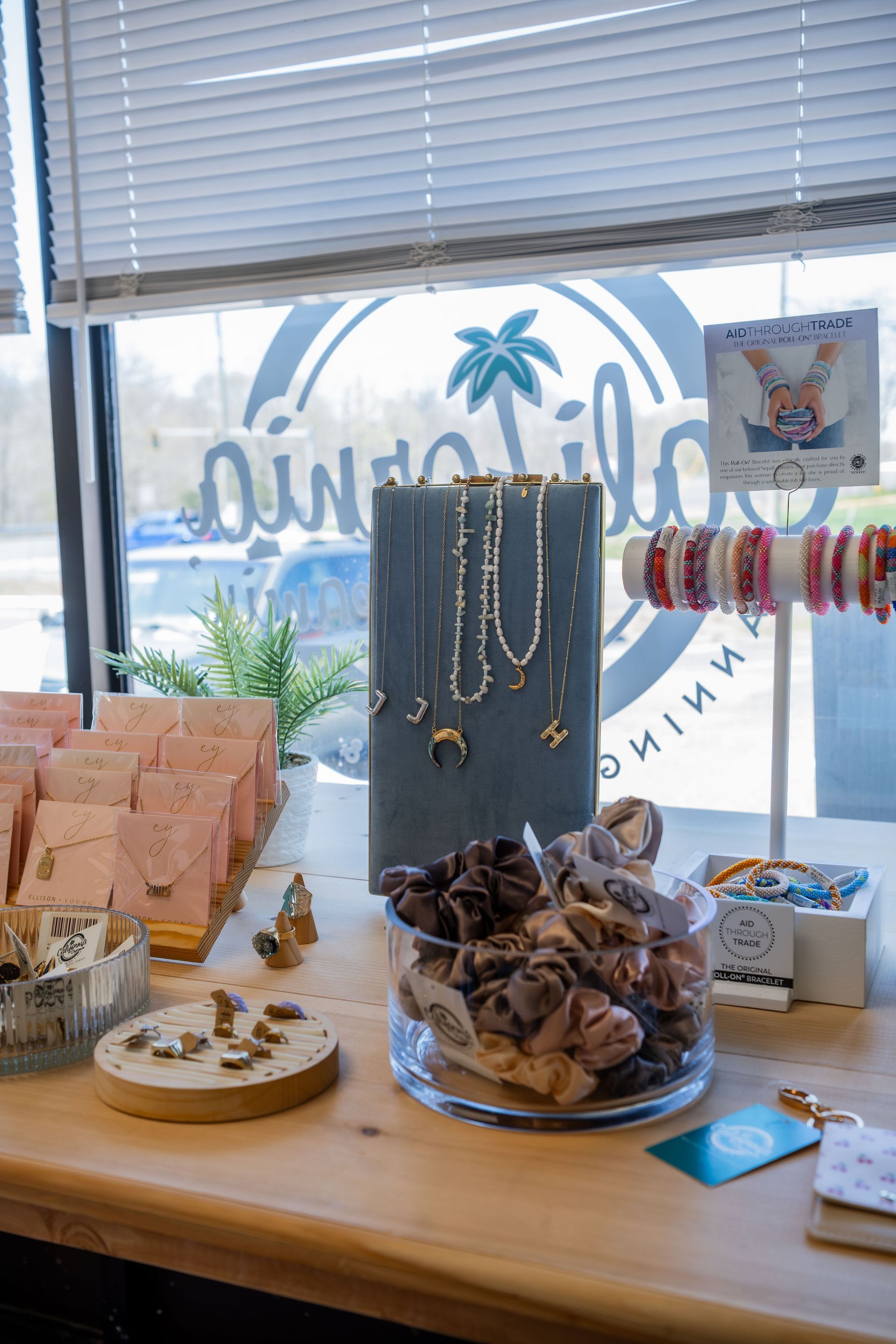 Jewelry display on a counter, with necklaces, bracelets, and hair accessories. The display is in front of a window with a logo.