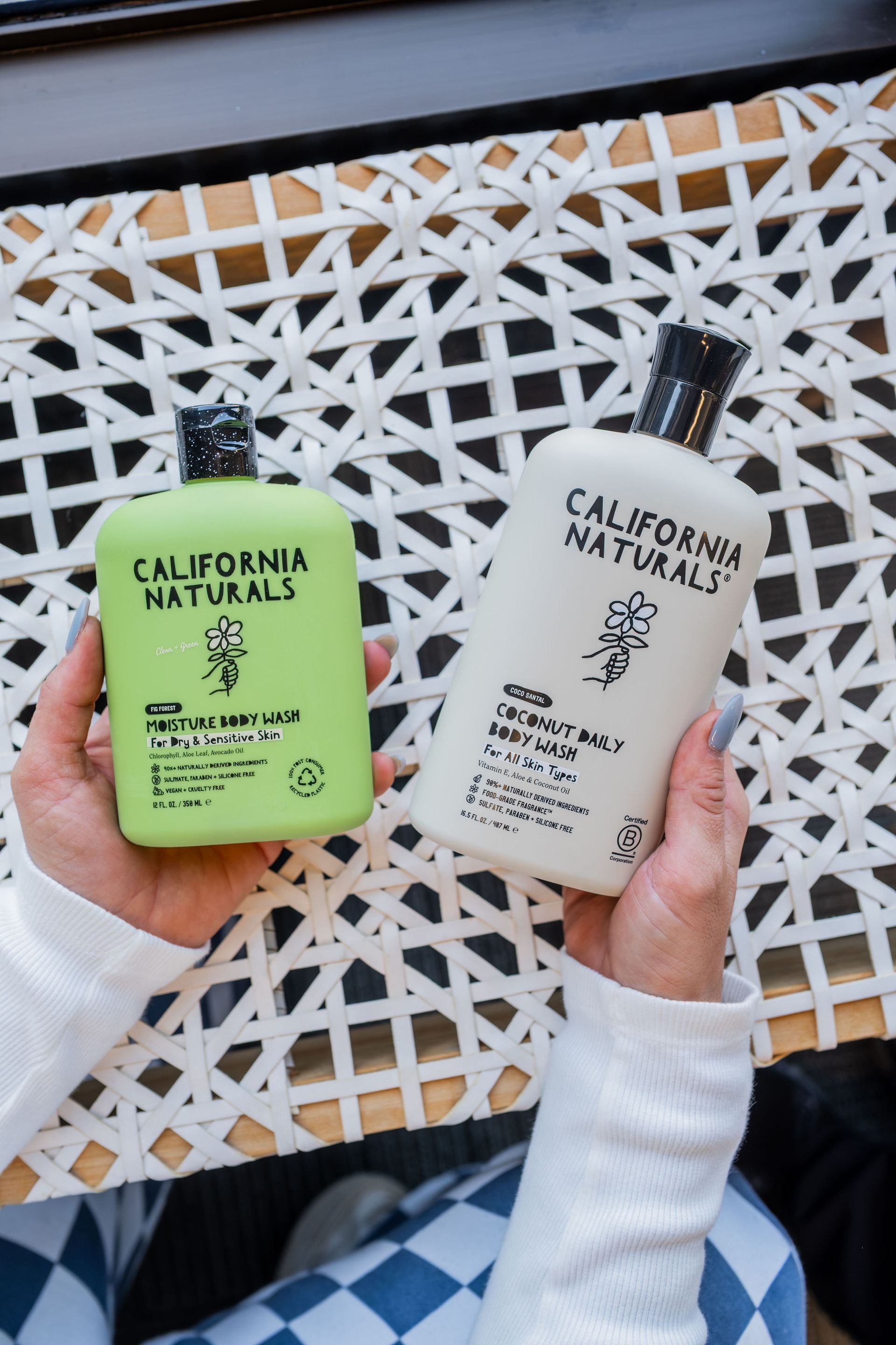 Two bottles of California Naturals shampoo held by a person over a white and beige wicker surface. One is green, the other white.