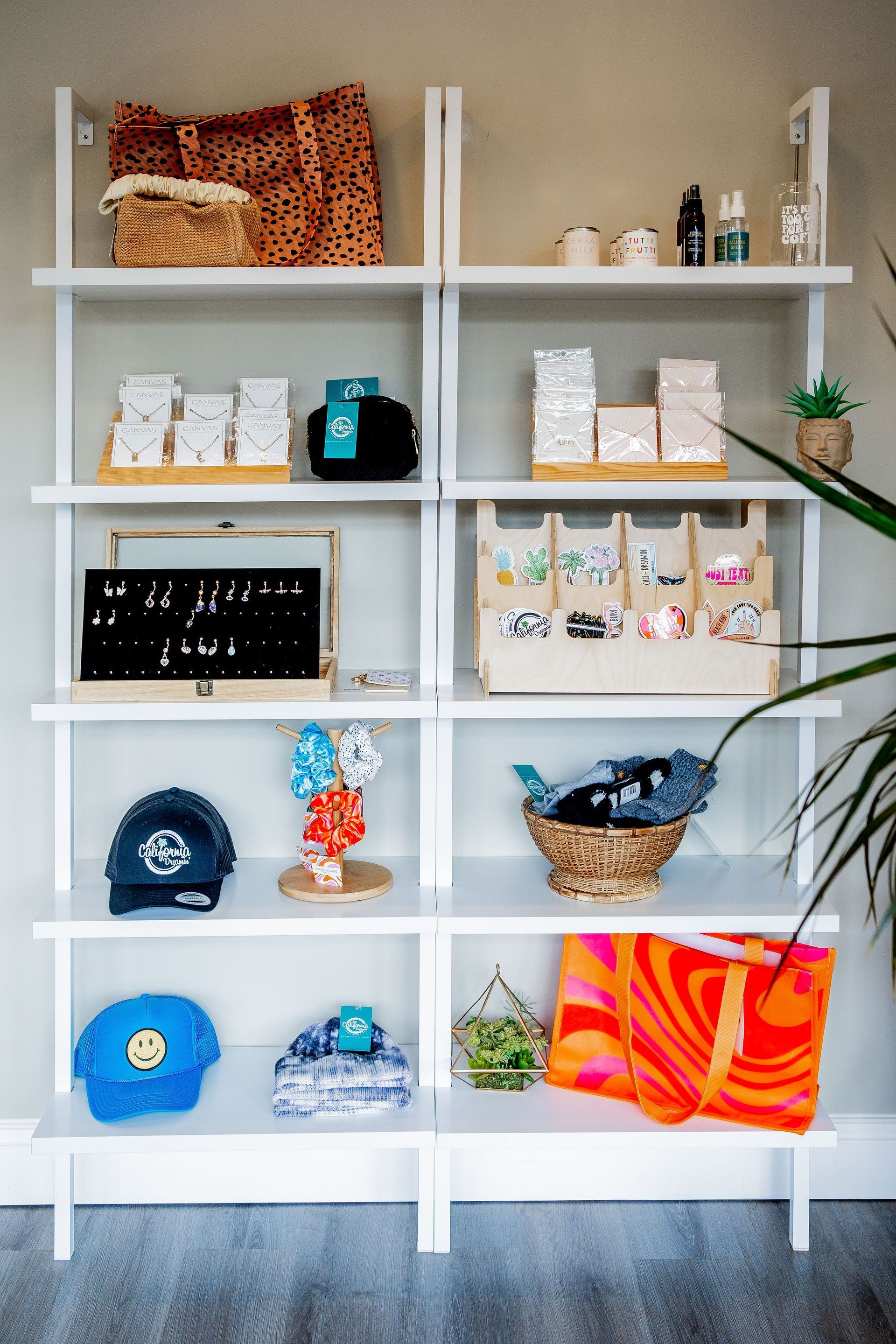 White shelving unit displaying various products: jewelry, hats, bags, and decorative items, against a light gray wall.