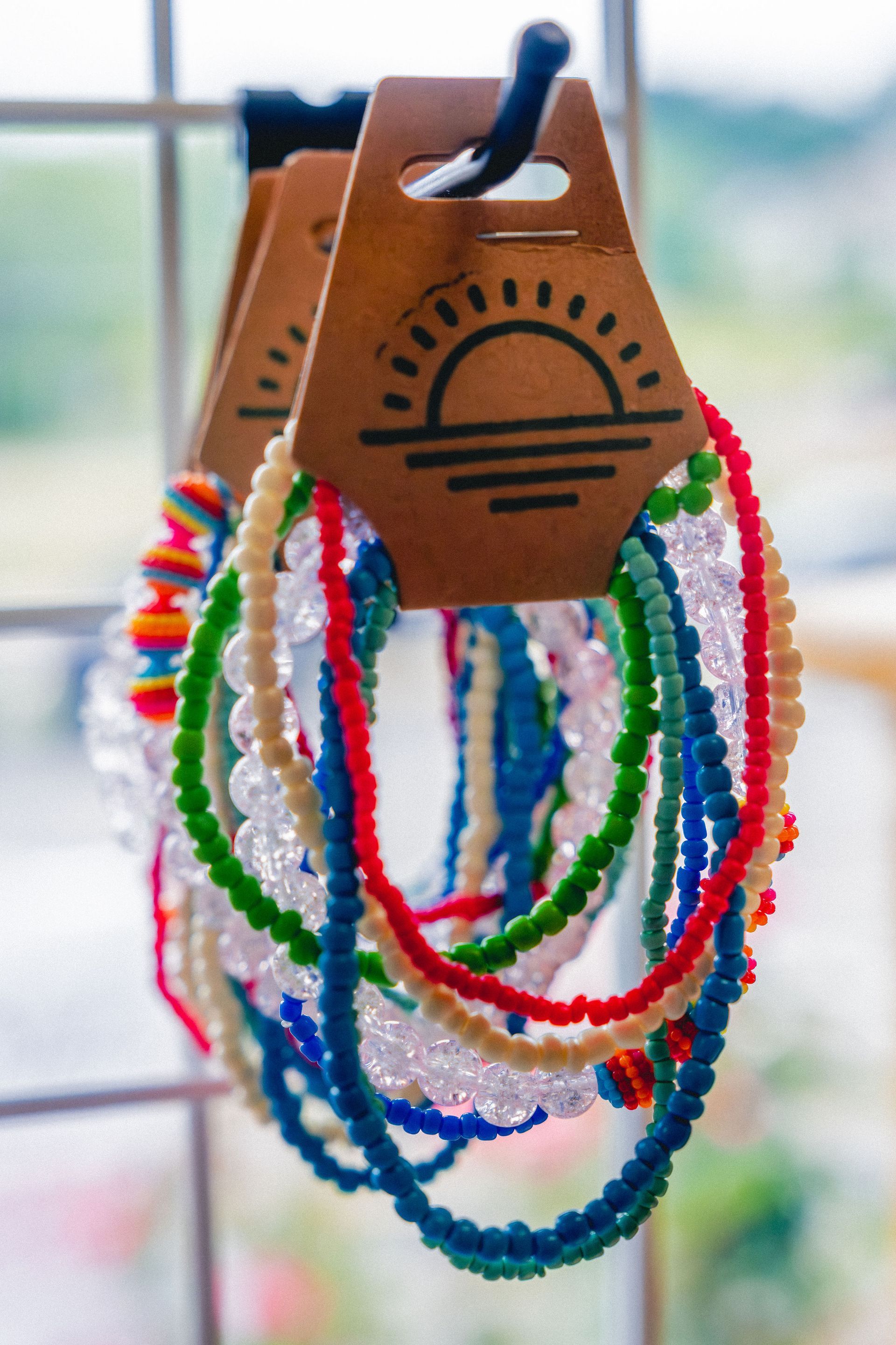 Colorful beaded bracelets hanging on a display, attached to cardboard tags with a sun logo.