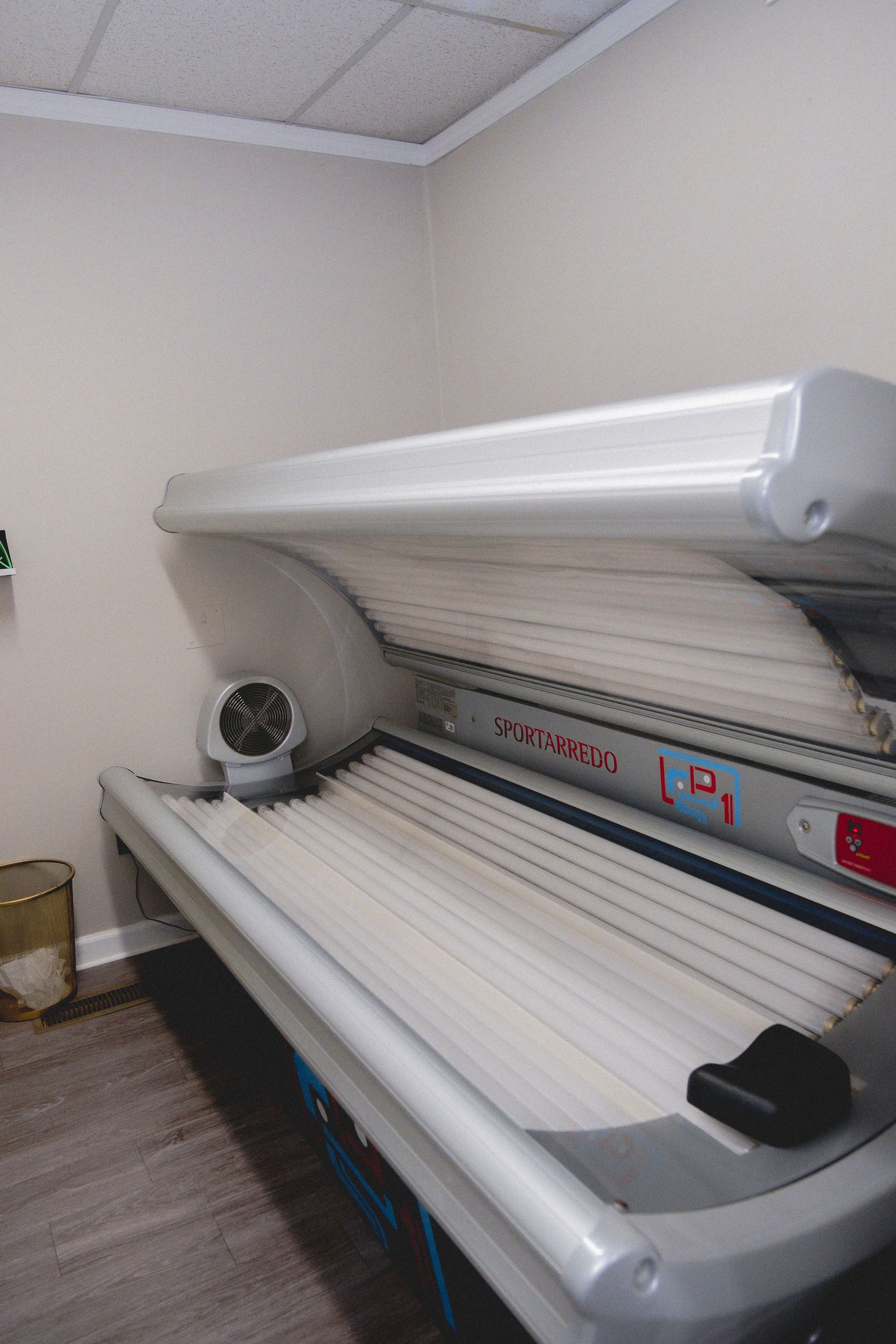 Tanning bed in a room, open, with lights. White and silver, fan visible.