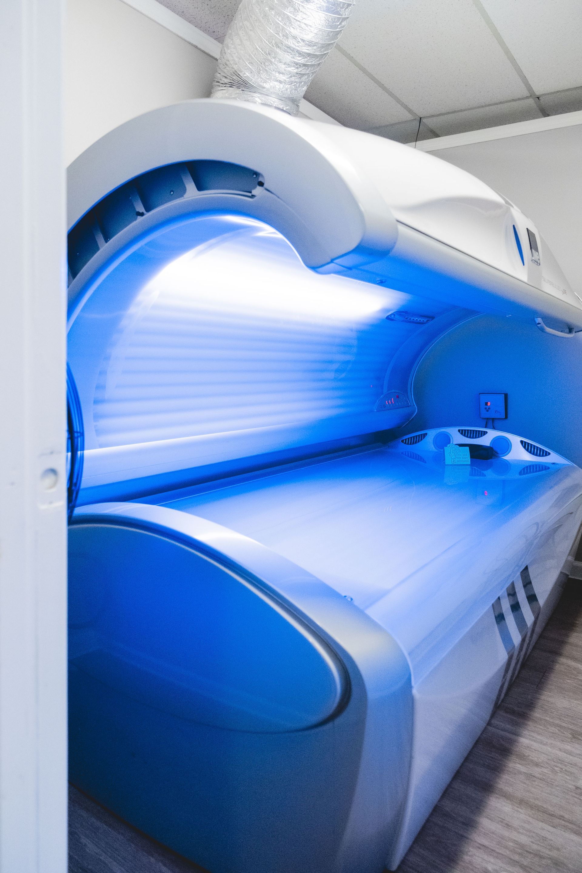 Tanning bed illuminated with blue light in a white-walled room.