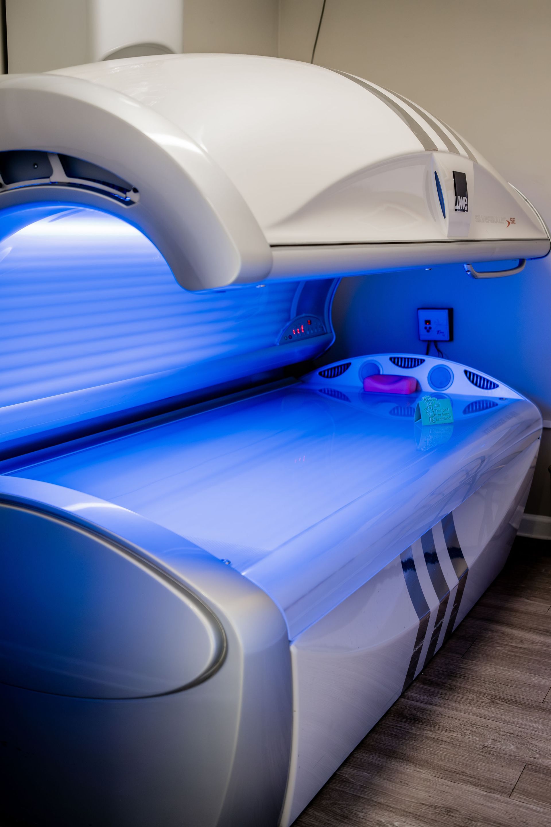 Tanning bed with blue interior lighting and white and silver exterior; in a room.