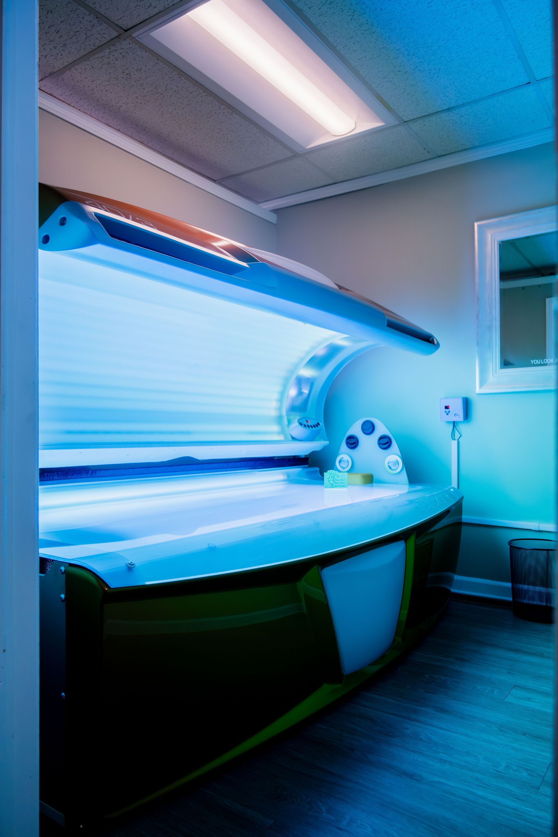 Tanning bed in a room with blue and green tones, bright lights, and a small window.
