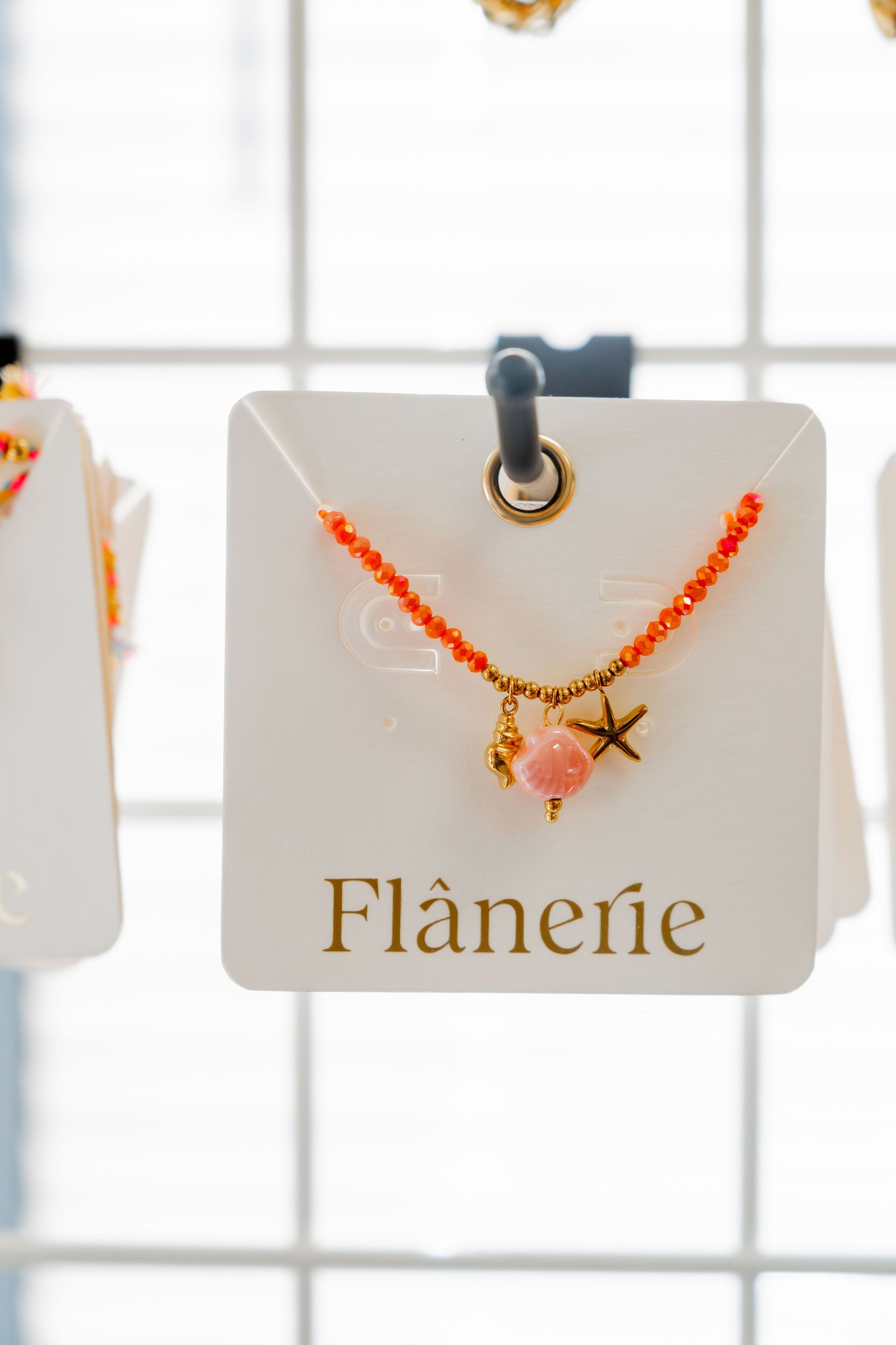 Orange beaded necklace with charms on a white card labeled 