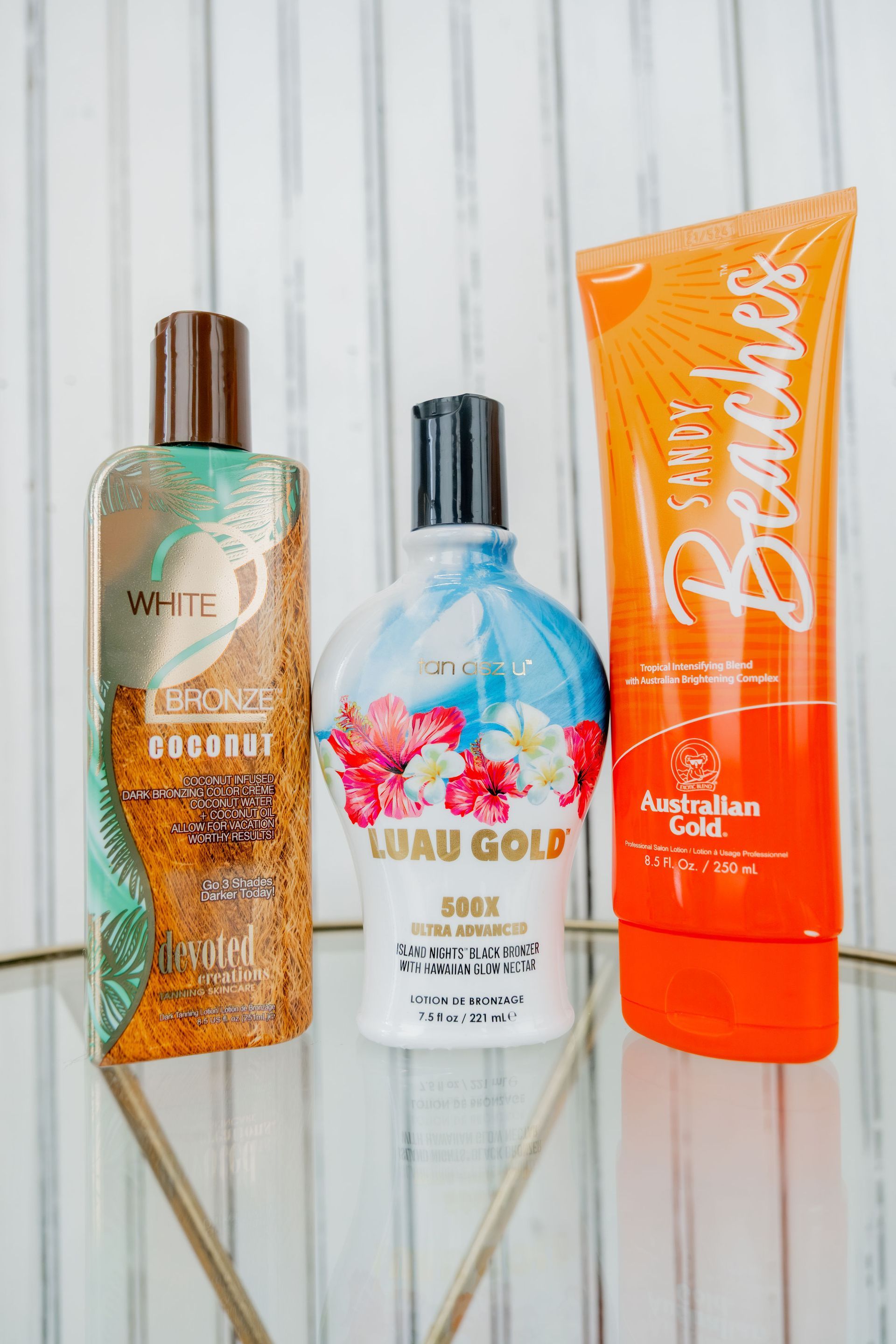 Three bottles of tanning lotion: brown and turquoise, white and floral, and orange tube labeled 