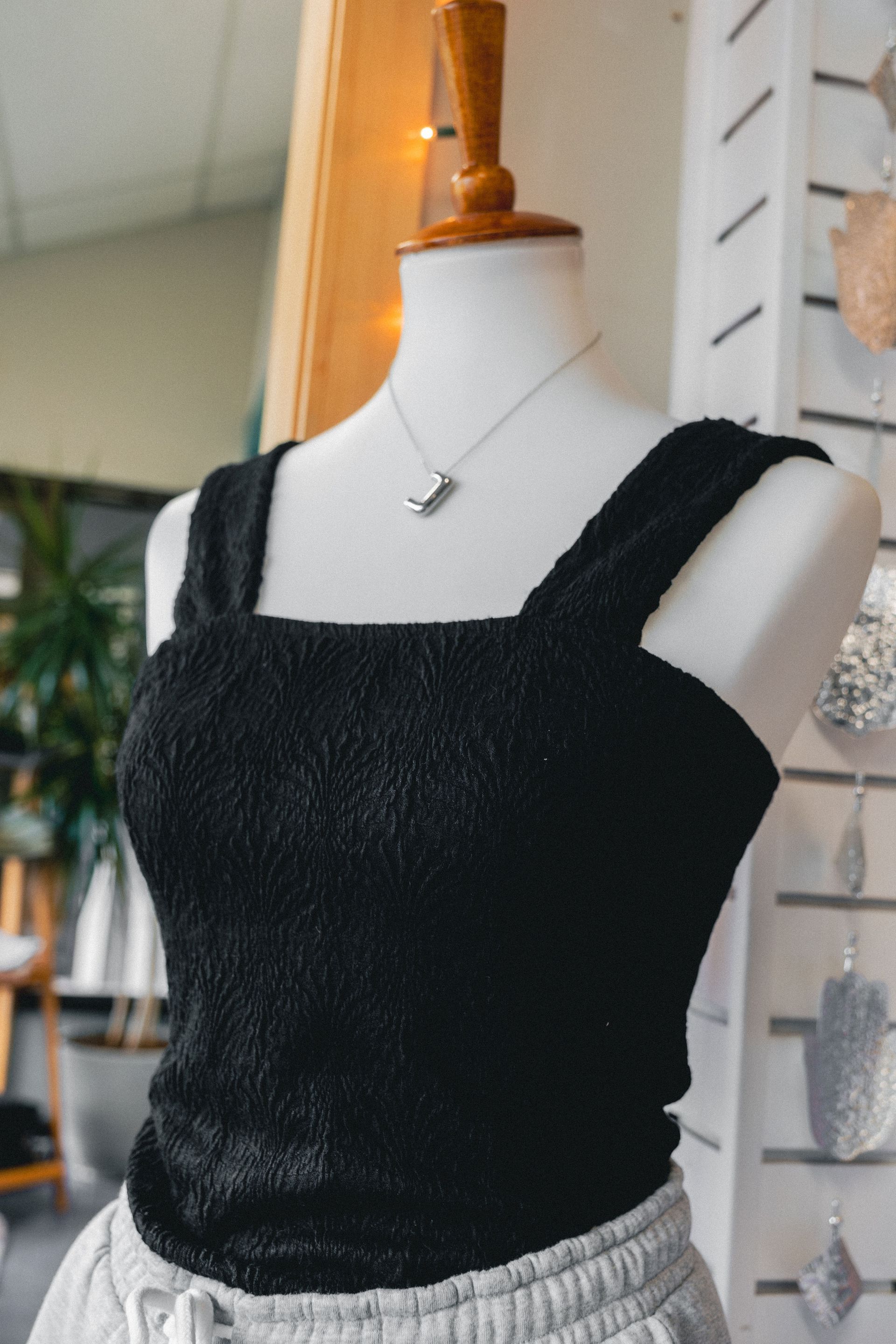 Black textured tank top on a mannequin. Silver necklace visible. Gray sweatpants below, displayed in a store setting.