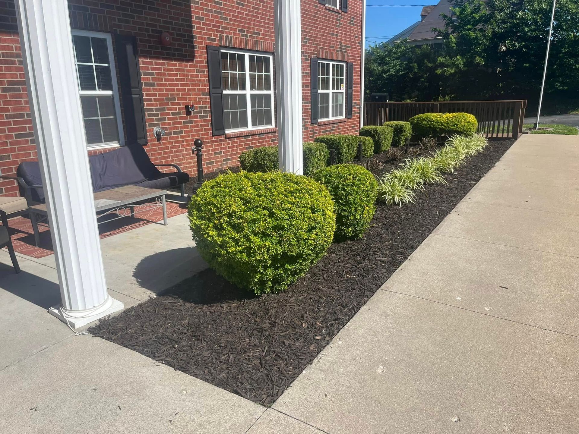 A brick building with a porch and bushes in front of it.