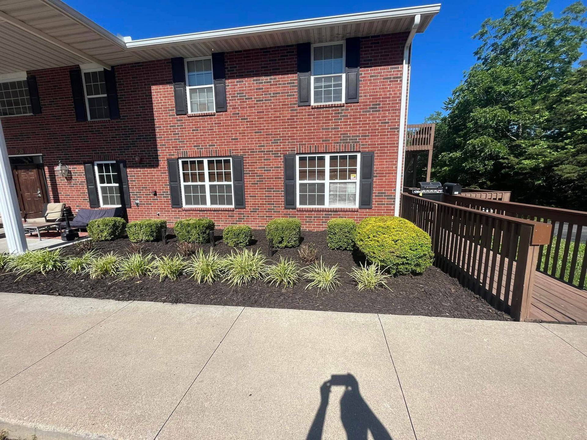 A brick house with black shutters and a fence in front of it.