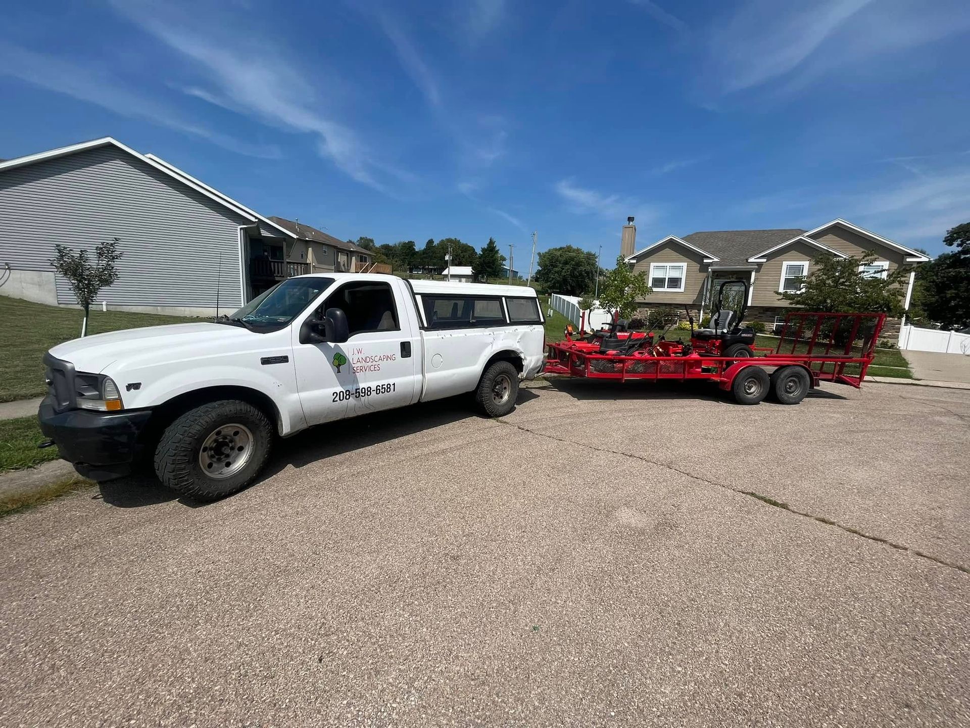 A white truck with a trailer attached to it is parked in front of a house.