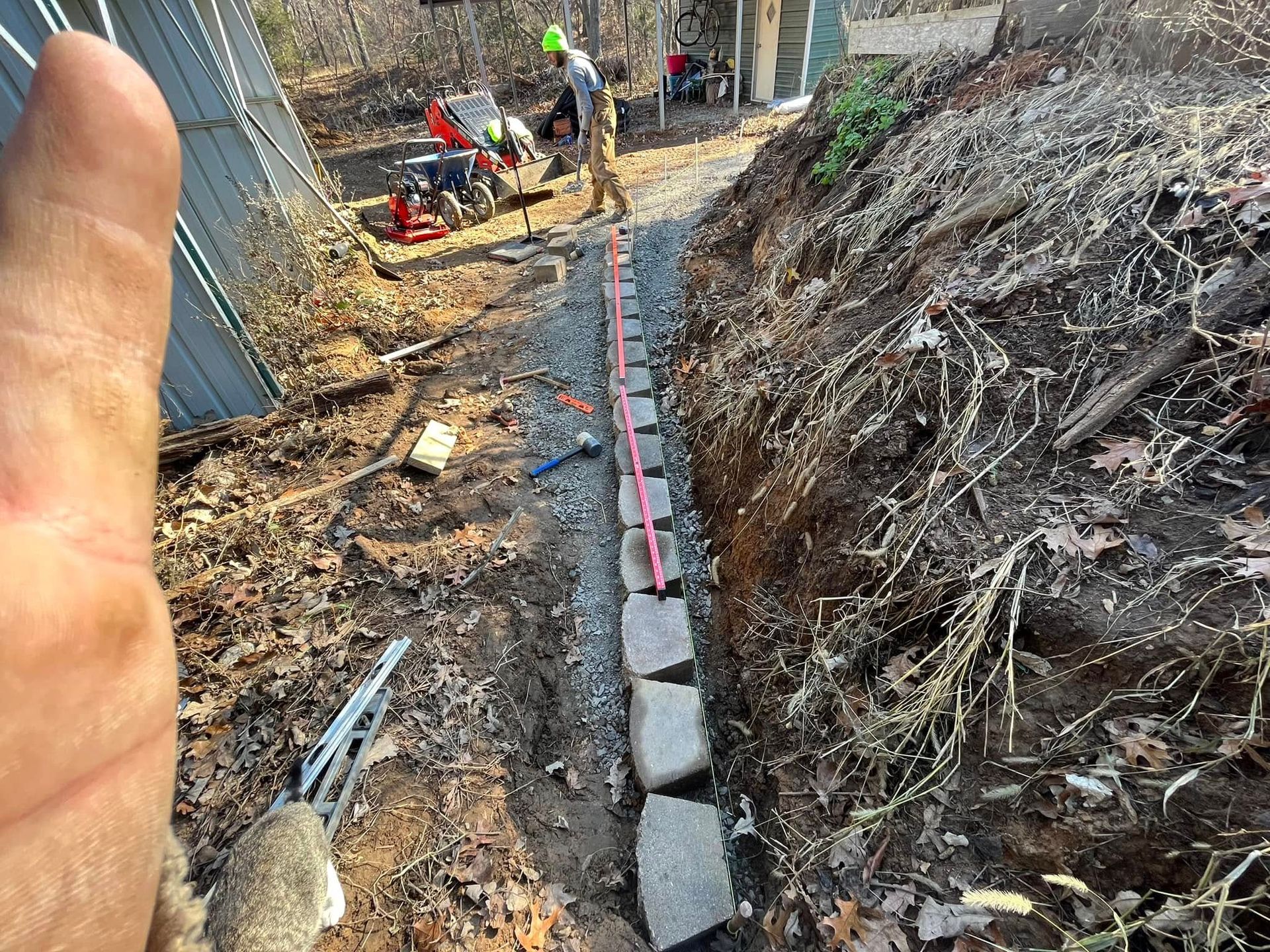 A person is standing in the dirt next to a brick wall.