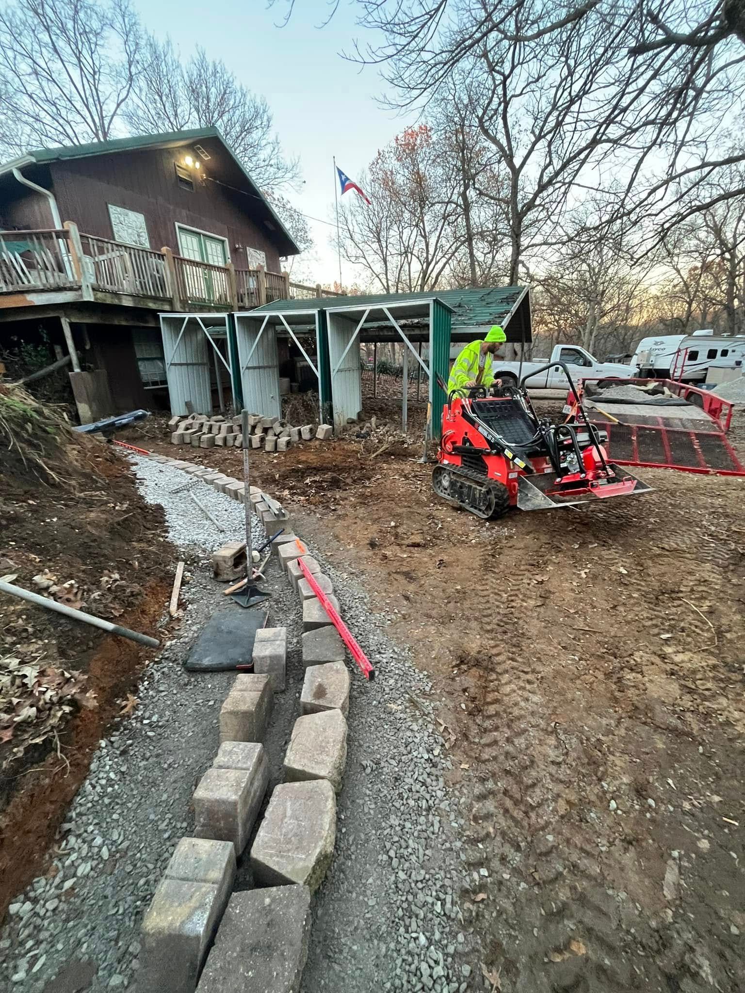 A man is riding a tractor on a dirt road in front of a house.