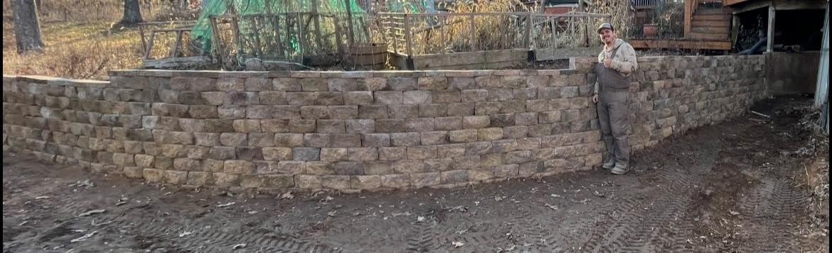 A man is standing in front of a stone wall.