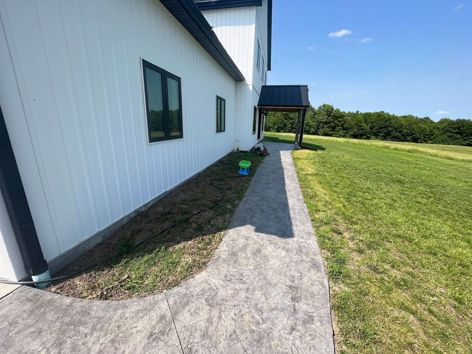 A house with a drain pipe on the side of it and a bush in front of it.