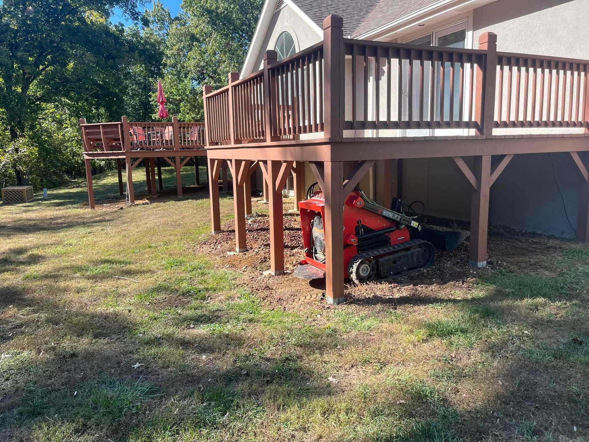 A red tractor is parked under a wooden deck.