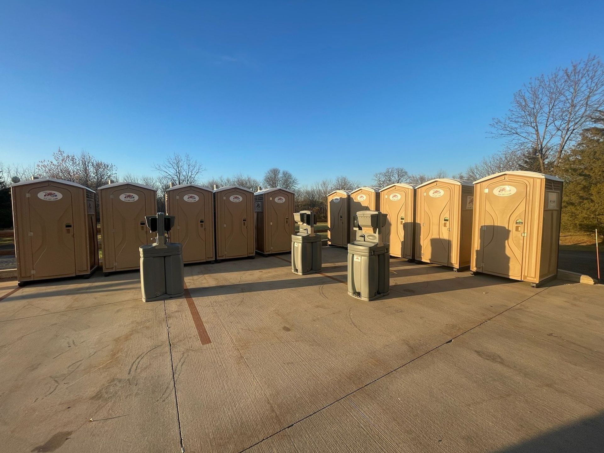 A row of portable toilets, one blue, the others gray, on a city sidewalk next to a street and bridge.