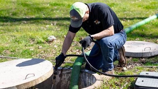 A man is kneeling down in the grass next to a septic tank.