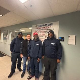 Four people in a room posing. A sign reads, 