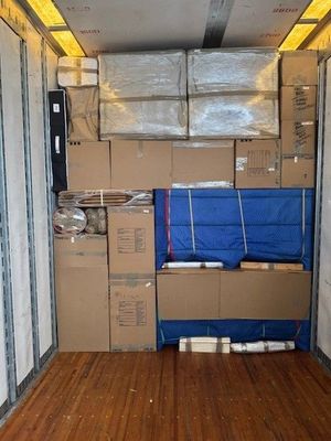 Boxes, furniture, and items fill the interior of a moving truck, secured with straps.