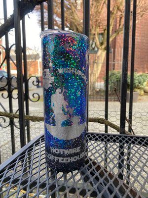 Glittery tumbler with silver Bigfoot graphic, text, blue, black, and white; sitting outside on a table.