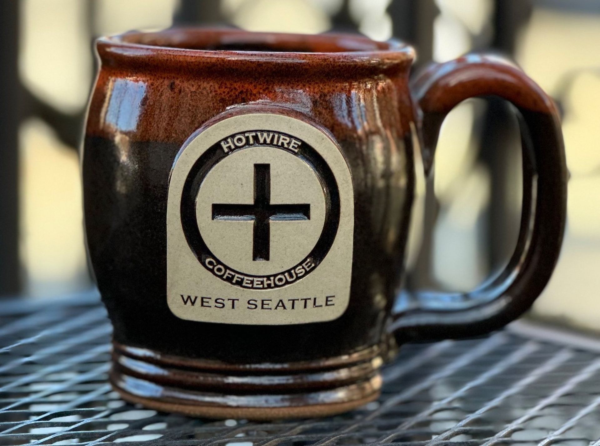 Coffee mug with Hotwire Coffeehouse logo, West Seattle. Brown ceramic, filled with coffee.