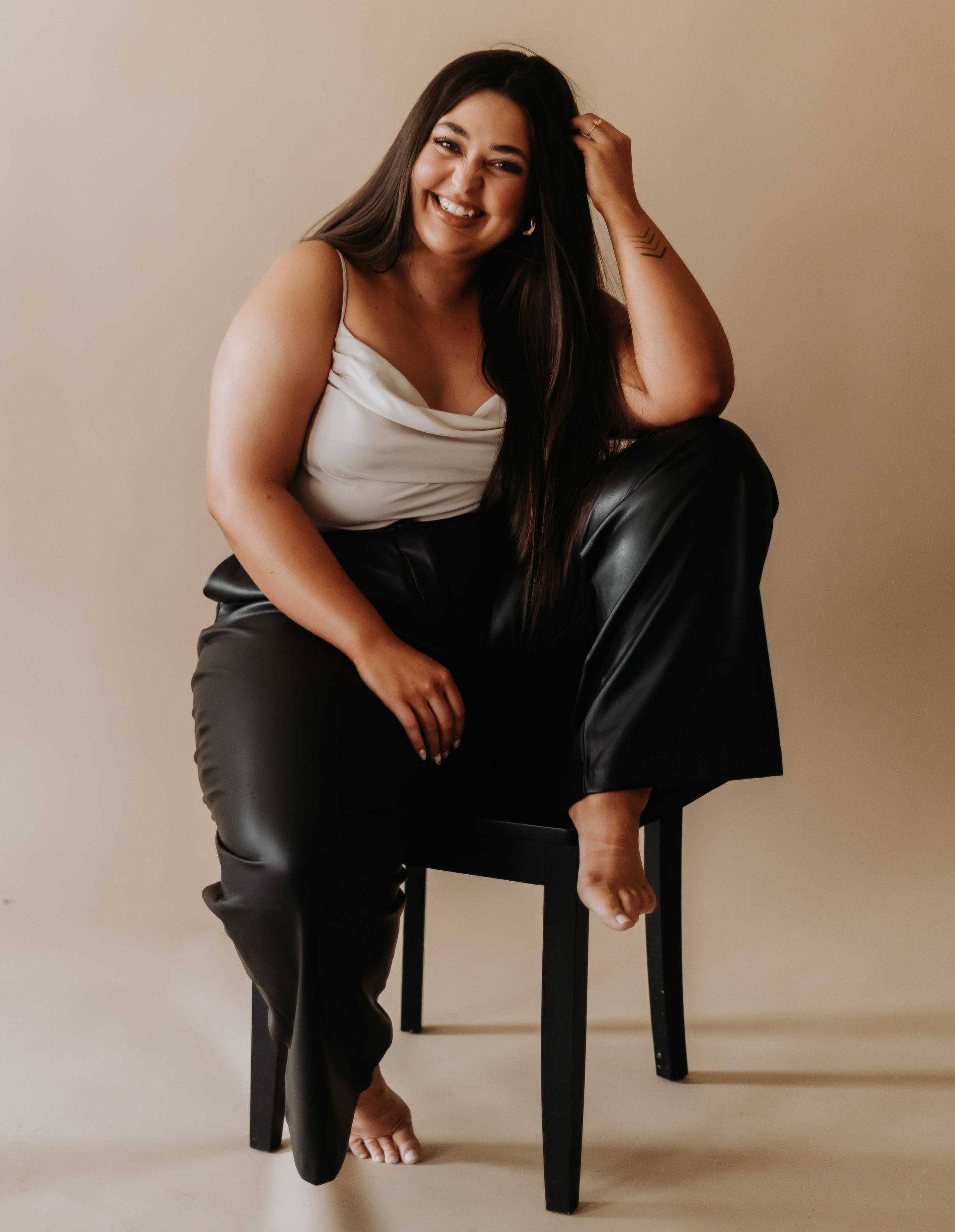 A woman is sitting on a chair with her legs crossed and smiling.