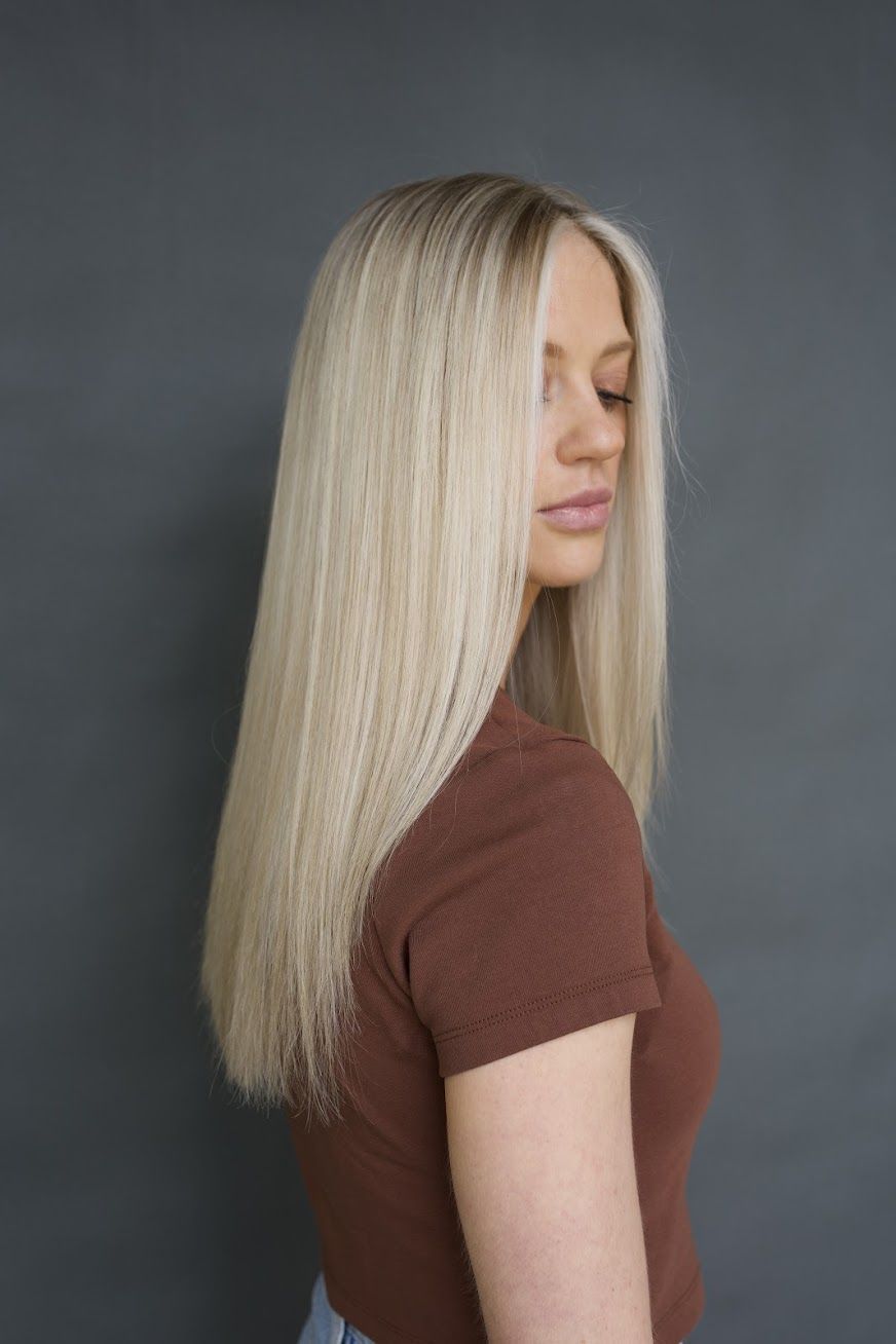 A woman with long blonde hair is wearing a brown shirt.