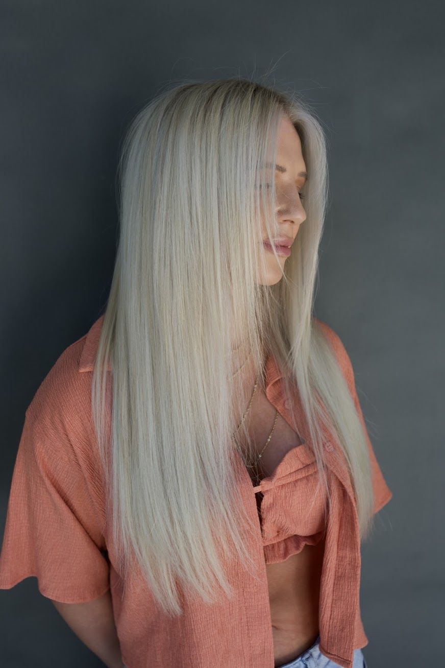 A woman with long blonde hair is wearing a pink shirt and jeans.