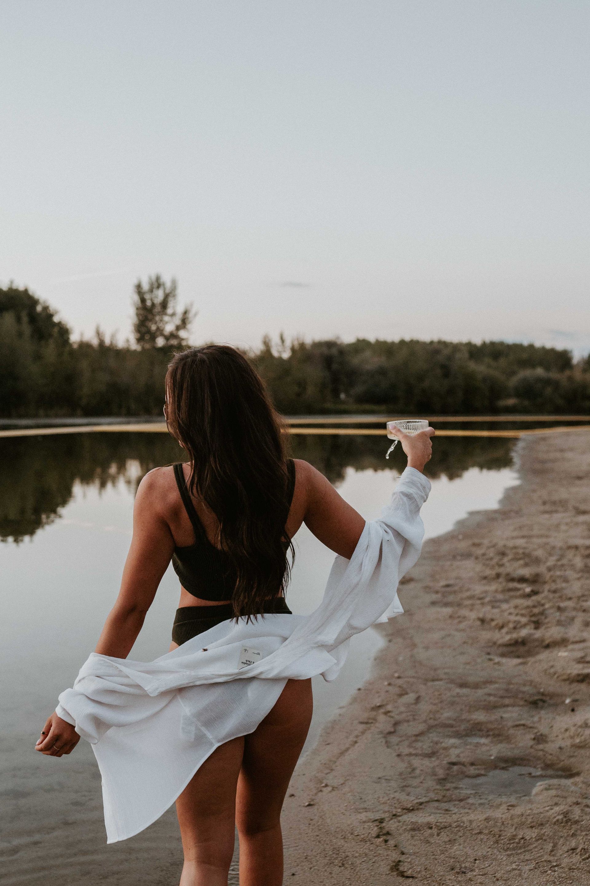 A woman in a bikini and a white shirt is standing on a beach.