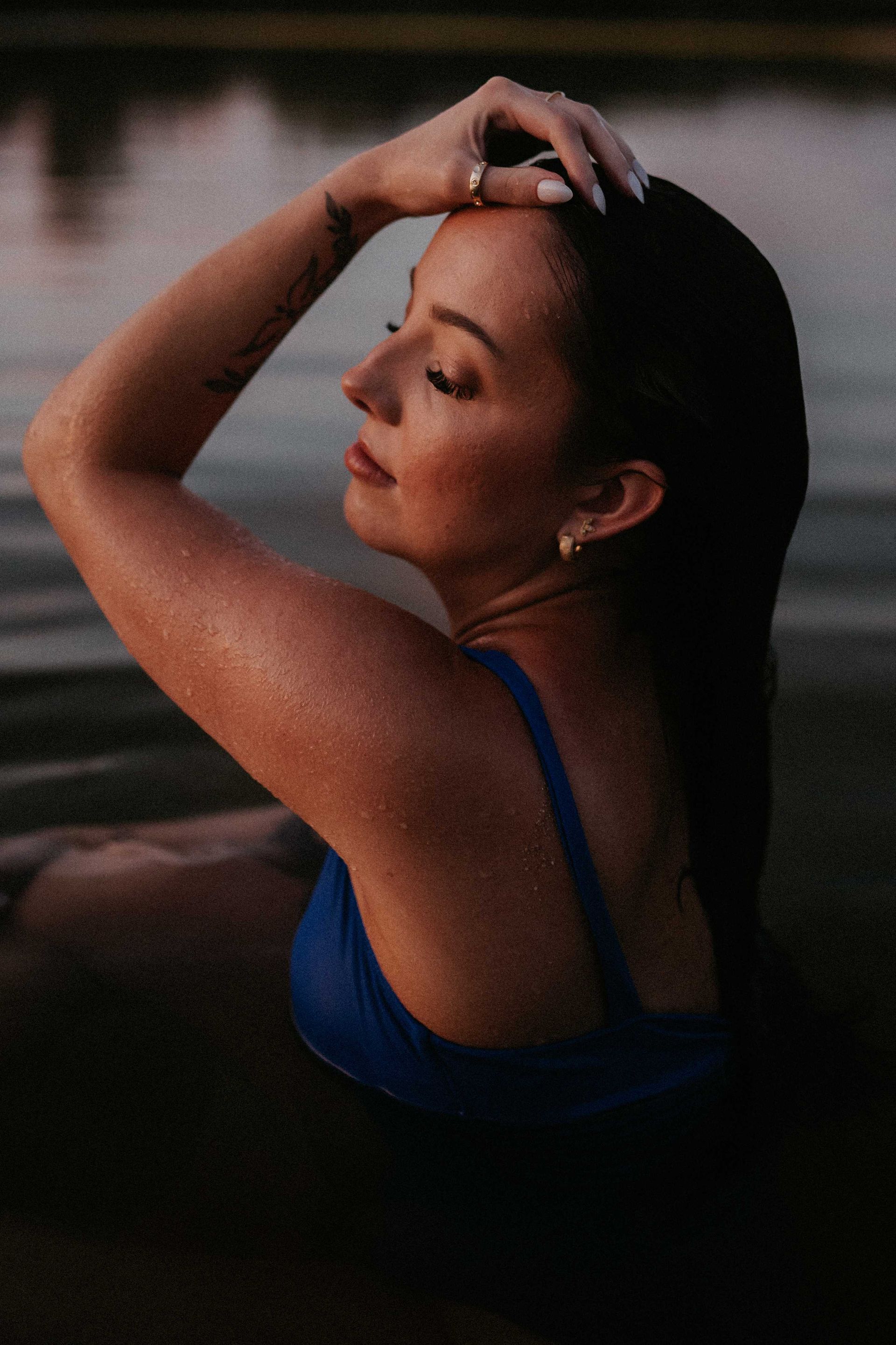 A woman in a blue bikini is sitting in the water with her eyes closed.