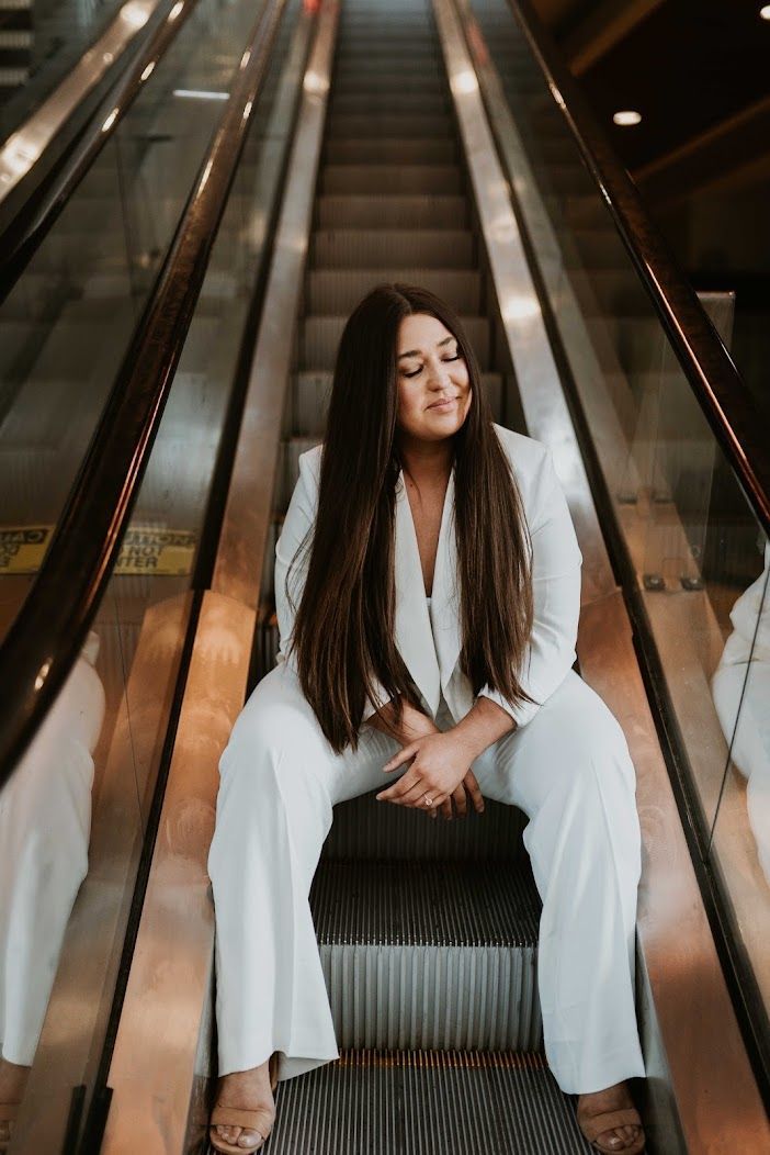 A woman in a white suit is sitting on an escalator.