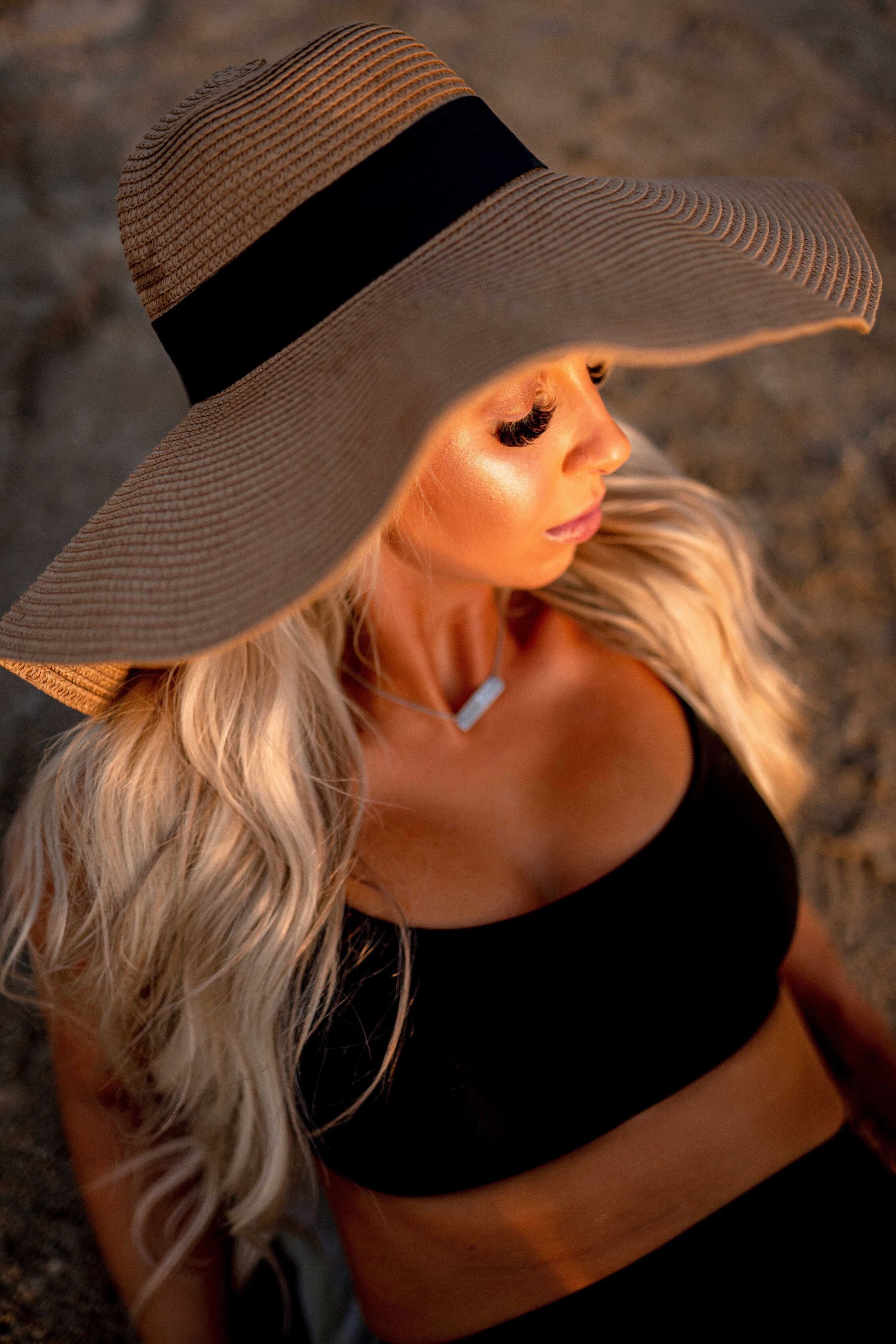 A woman wearing a hat and a black top is sitting on the beach.