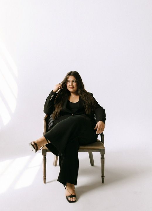 A woman is sitting on a stool with her legs crossed and smiling.