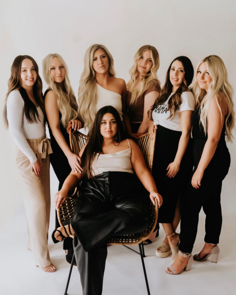 A group of women are standing around a woman sitting in a chair.