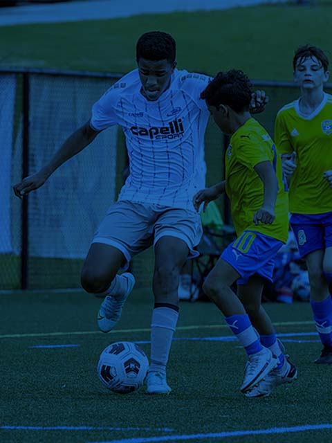 Soccer players in action on field. One in white shirt with ball, another in green shirt attempting to defend.